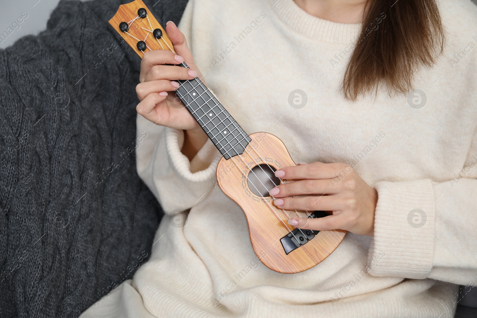 Photo of Woman playing ukulele in armchair at home, closeup