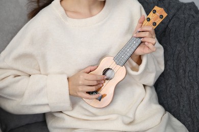 Photo of Woman playing ukulele in armchair at home, closeup