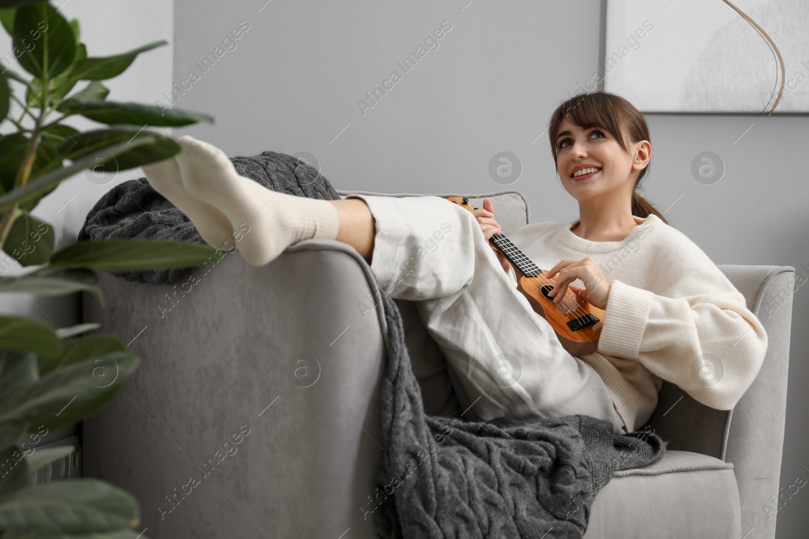 Photo of Happy woman playing ukulele in armchair at home