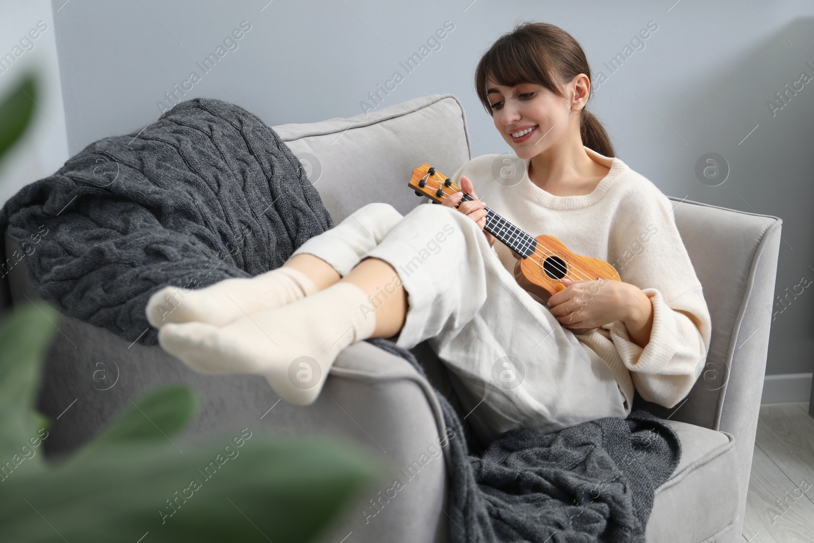 Photo of Happy woman playing ukulele in armchair at home