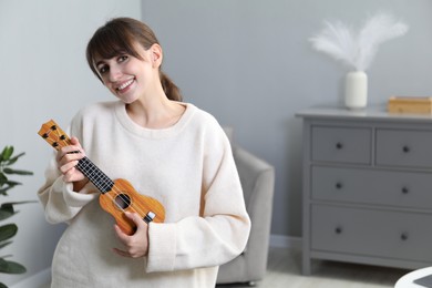 Photo of Happy young woman playing ukulele at home, space for text