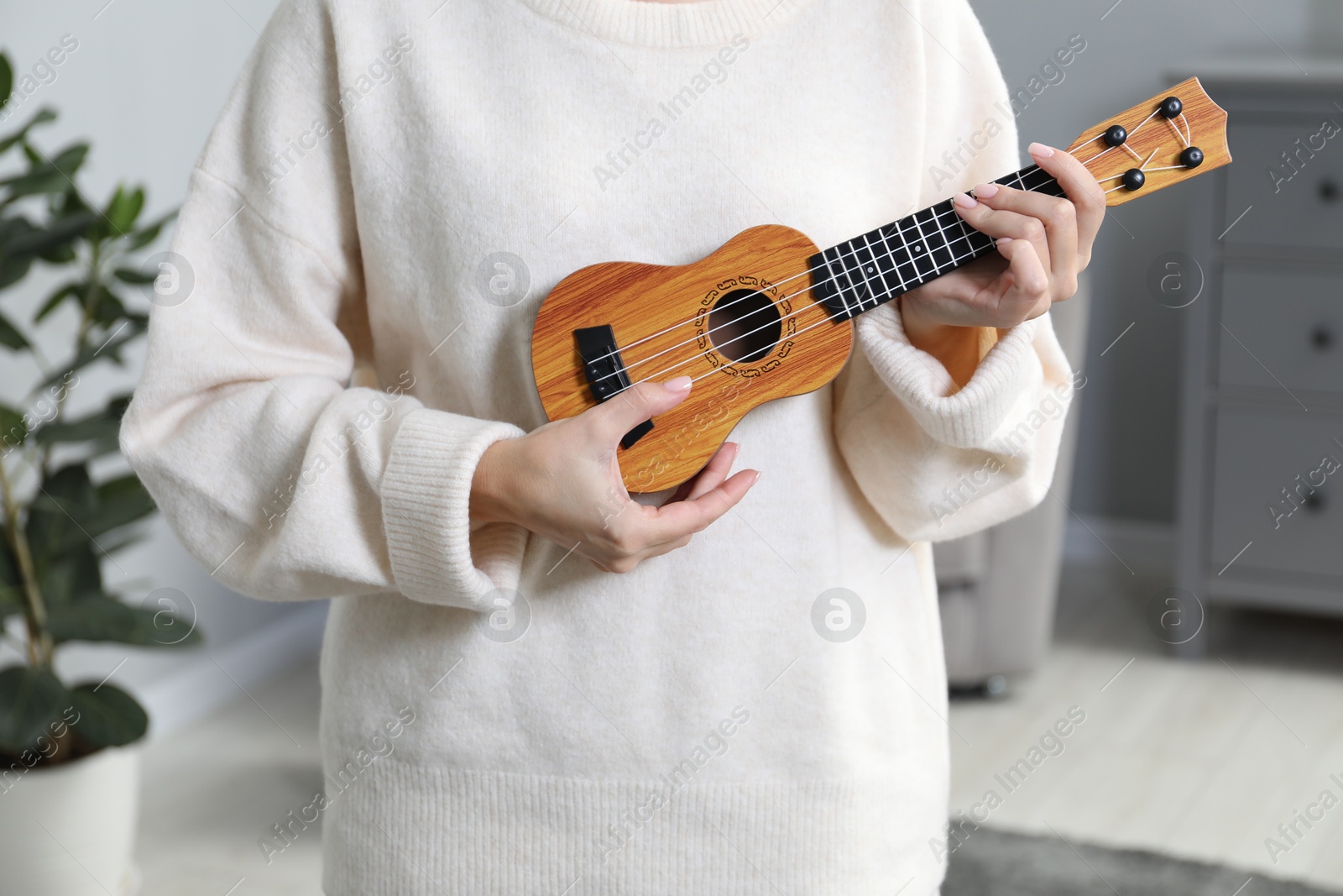 Photo of Woman playing ukulele at home, closeup view