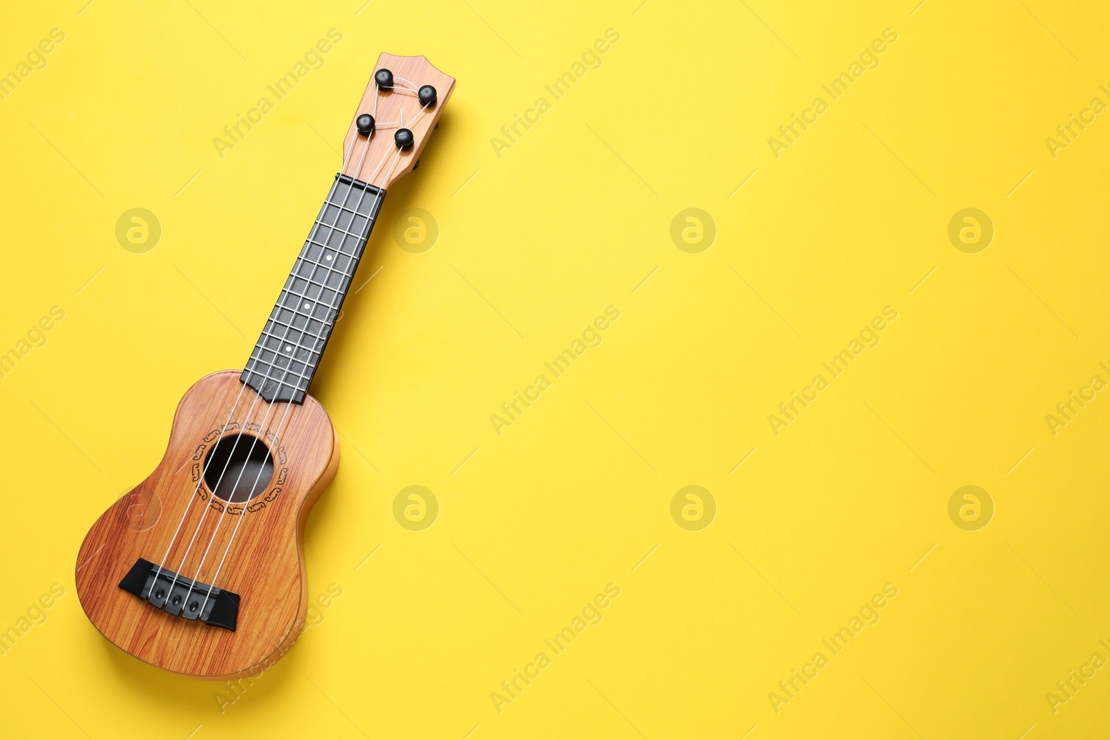 Photo of One ukulele on yellow background, top view. Space for text