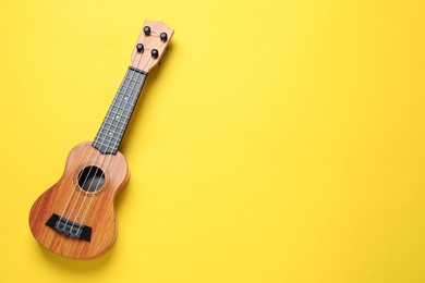 Photo of One ukulele on yellow background, top view. Space for text