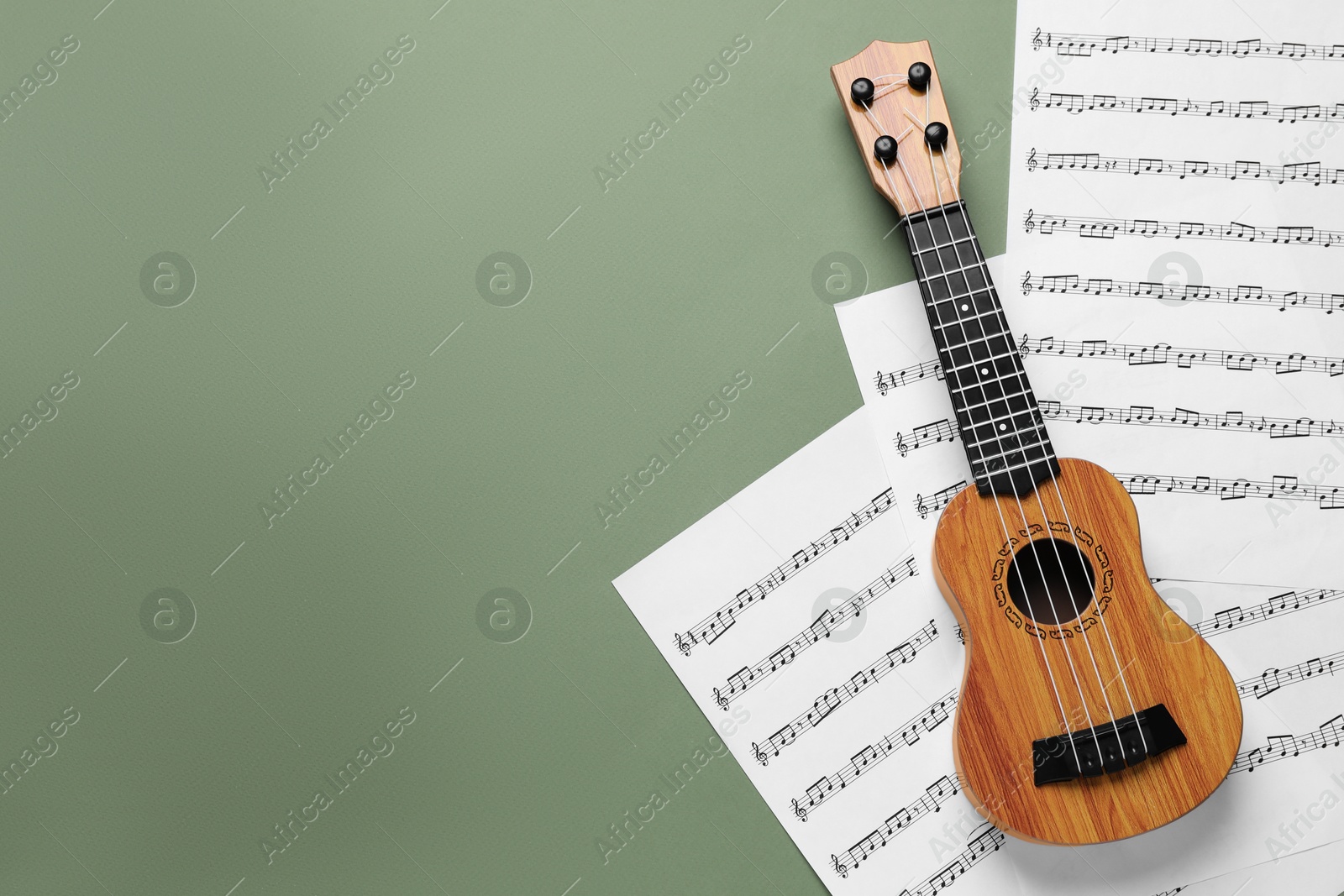 Photo of Ukulele and music sheets on green background, top view. Space for text