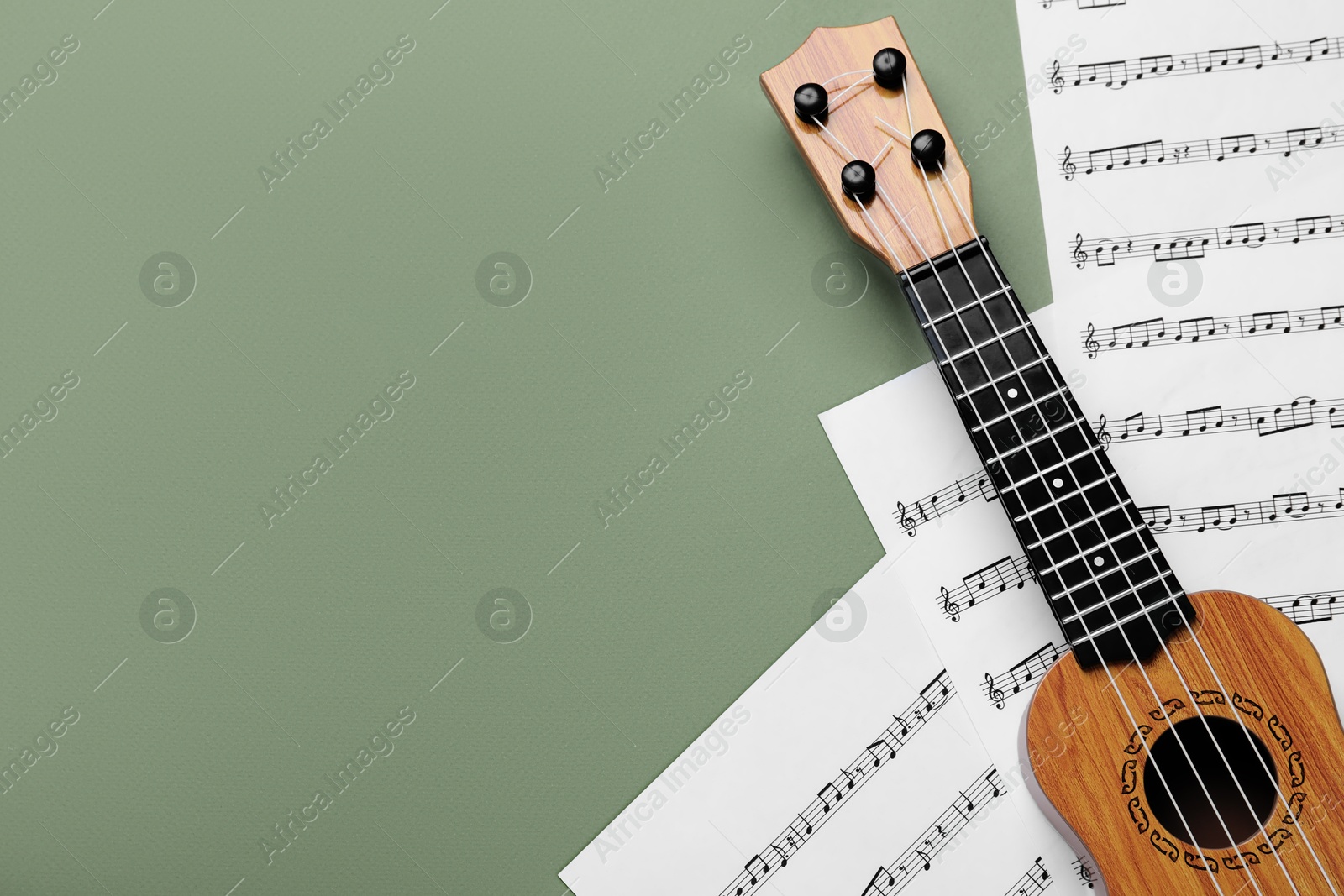 Photo of Ukulele and music sheets on green background, top view. Space for text