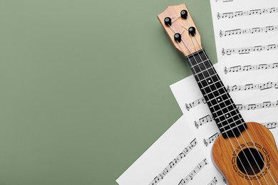 Photo of Ukulele and music sheets on green background, top view. Space for text