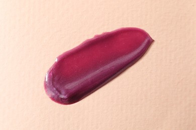 Photo of Sample of purple lipgloss on beige background, top view