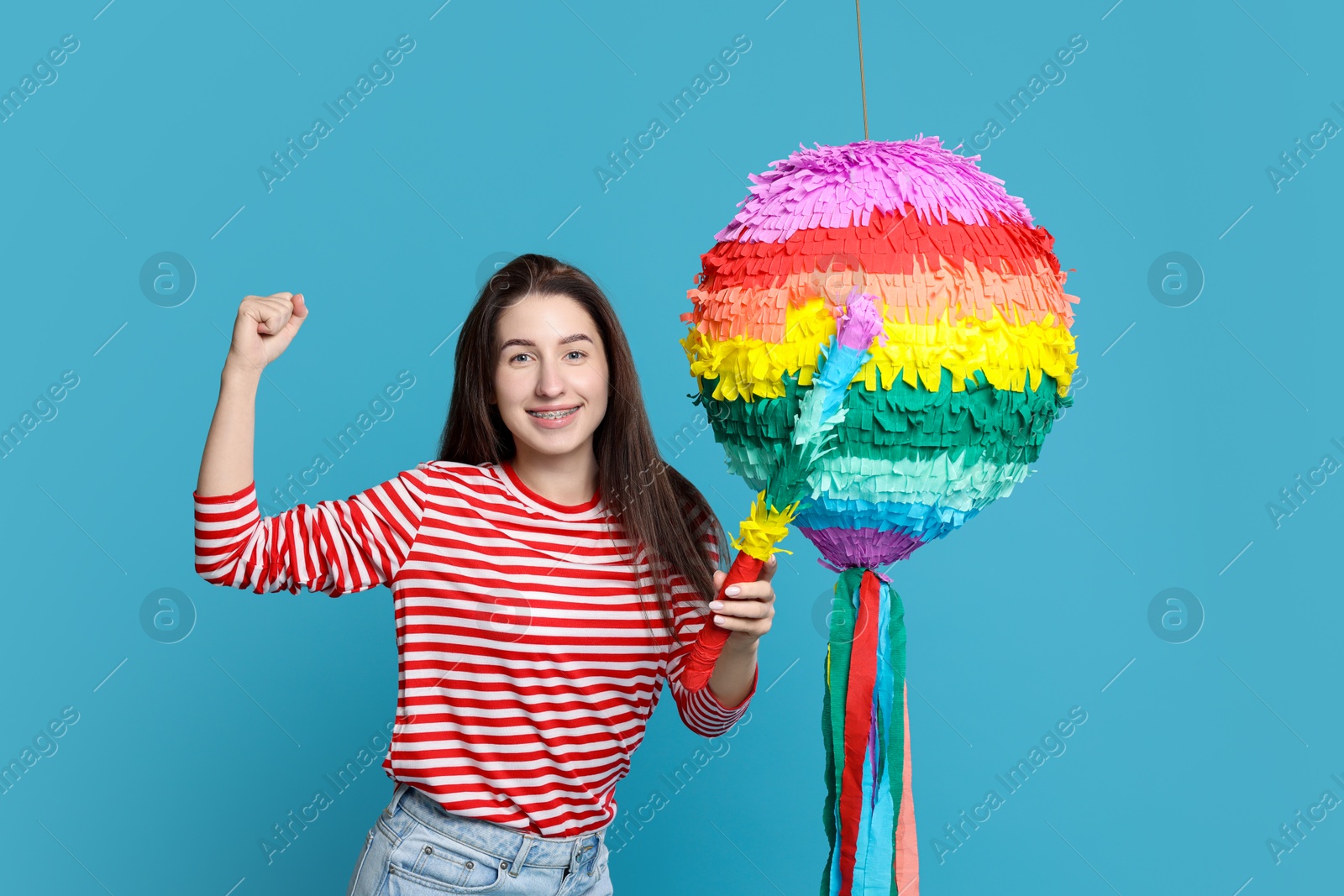 Photo of Happy woman with colorful pinata and stick on light blue background