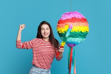 Photo of Happy woman with colorful pinata and stick on light blue background