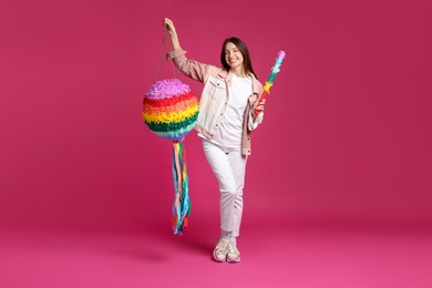 Photo of Happy woman with colorful pinata and stick on pink background