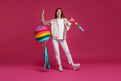 Photo of Happy woman with colorful pinata and stick on pink background