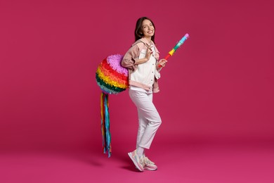 Photo of Happy woman with colorful pinata and stick on pink background