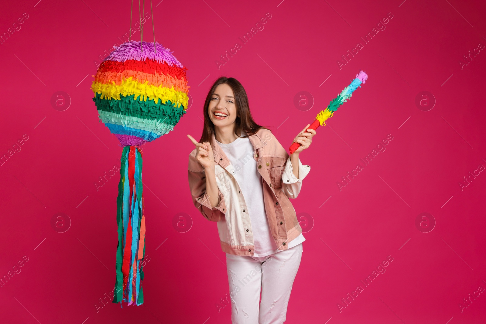 Photo of Happy woman with colorful pinata and stick on pink background