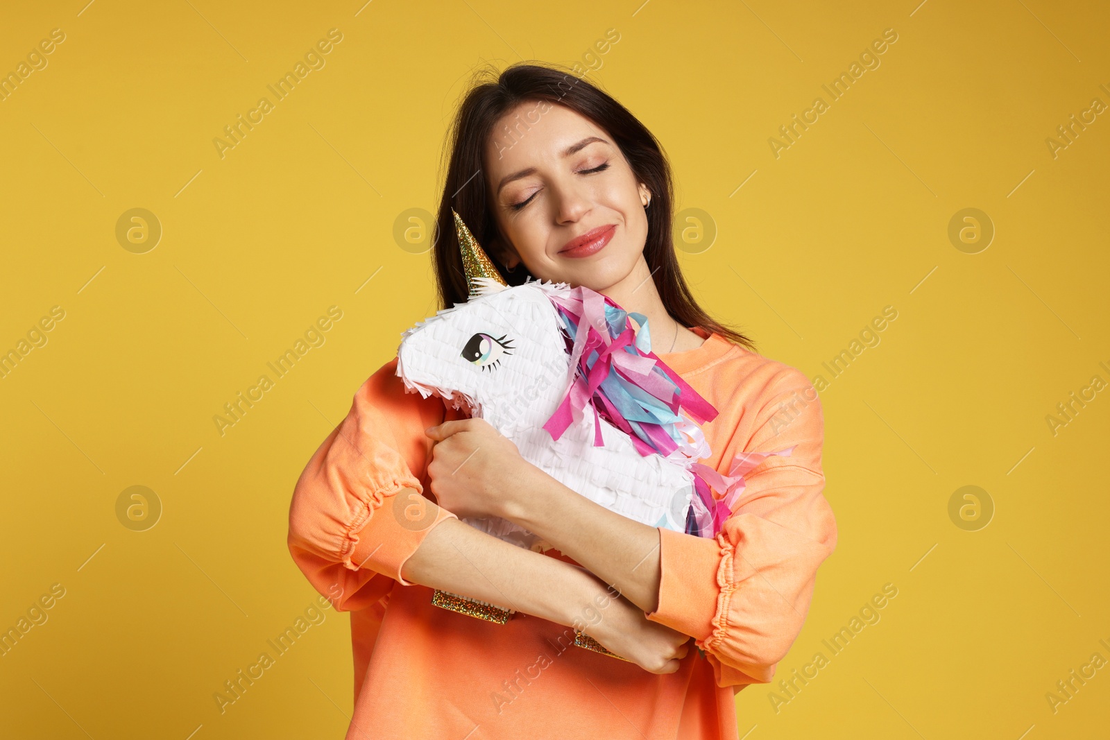 Photo of Beautiful woman with unicorn shaped pinata on yellow background