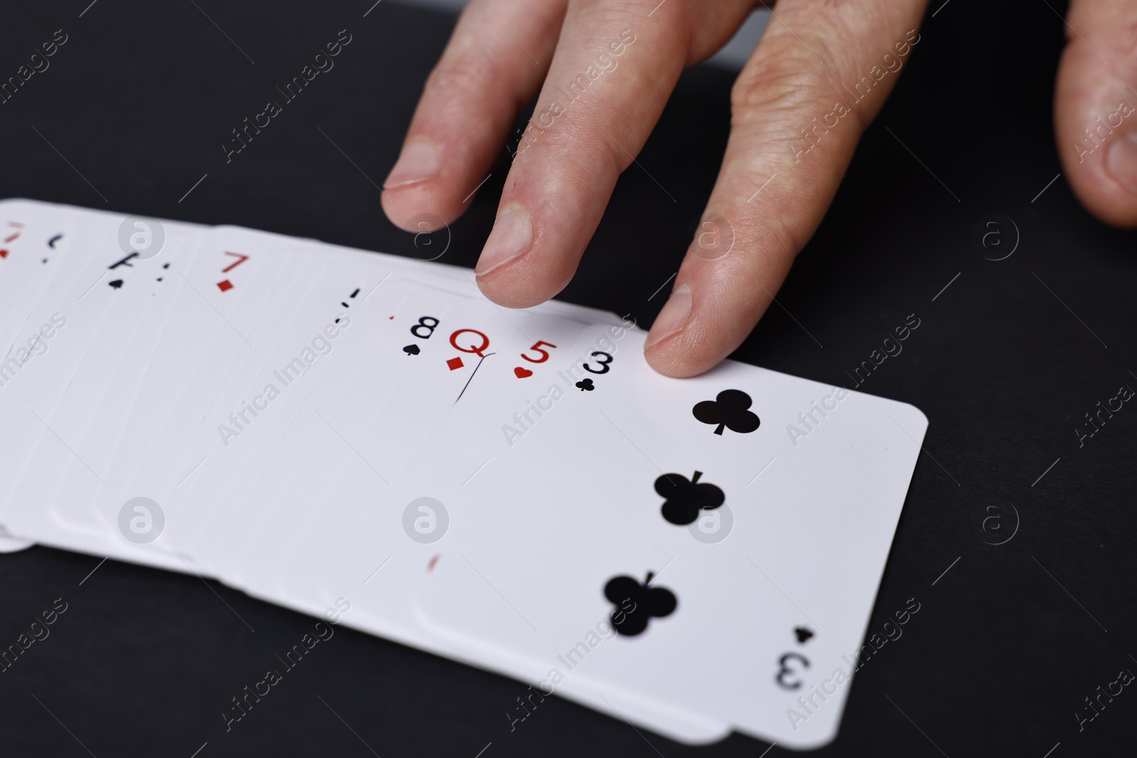 Photo of Illusionist with playing cards at black table, closeup