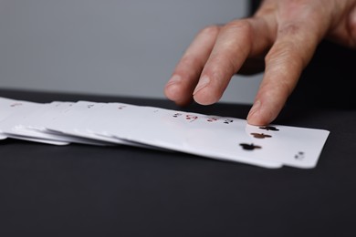 Photo of Illusionist with playing cards at black table, closeup