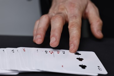 Photo of Illusionist with playing cards at black table, closeup