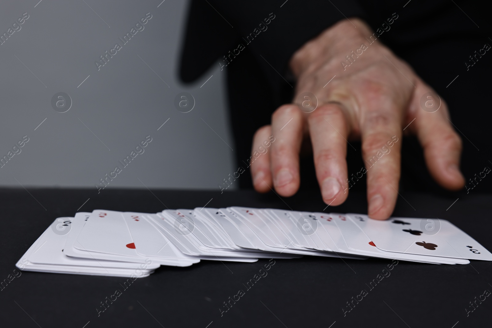 Photo of Illusionist with playing cards at black table, closeup