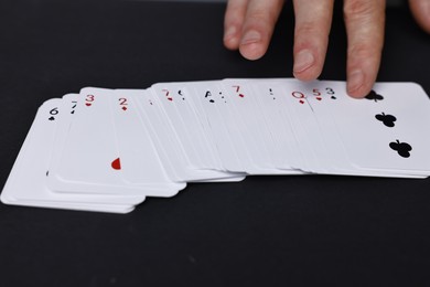 Photo of Illusionist with playing cards at black table, closeup