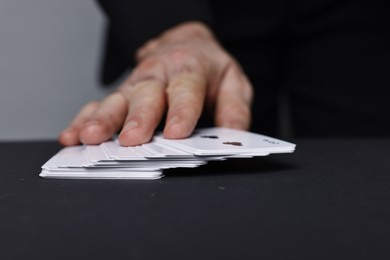 Photo of Illusionist with playing cards at black table, closeup