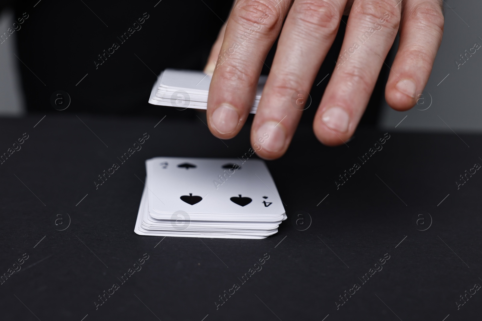 Photo of Illusionist with playing cards at black table, closeup