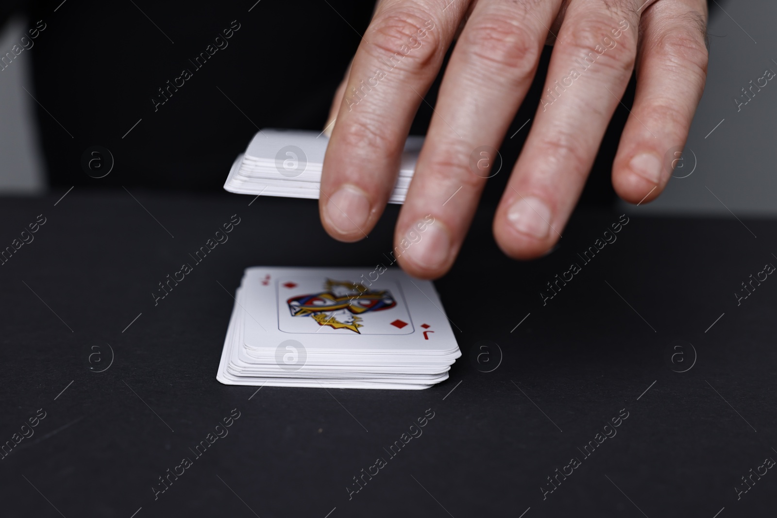 Photo of Illusionist with playing cards at black table, closeup