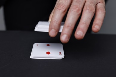 Photo of Illusionist with playing cards at black table, closeup