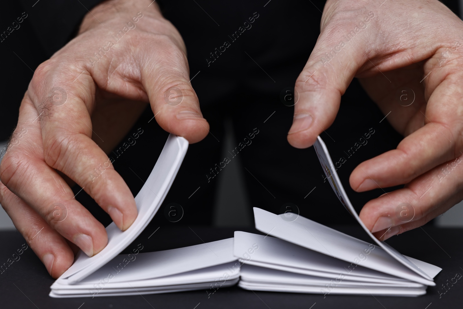 Photo of Illusionist shuffling playing cards at black table, closeup