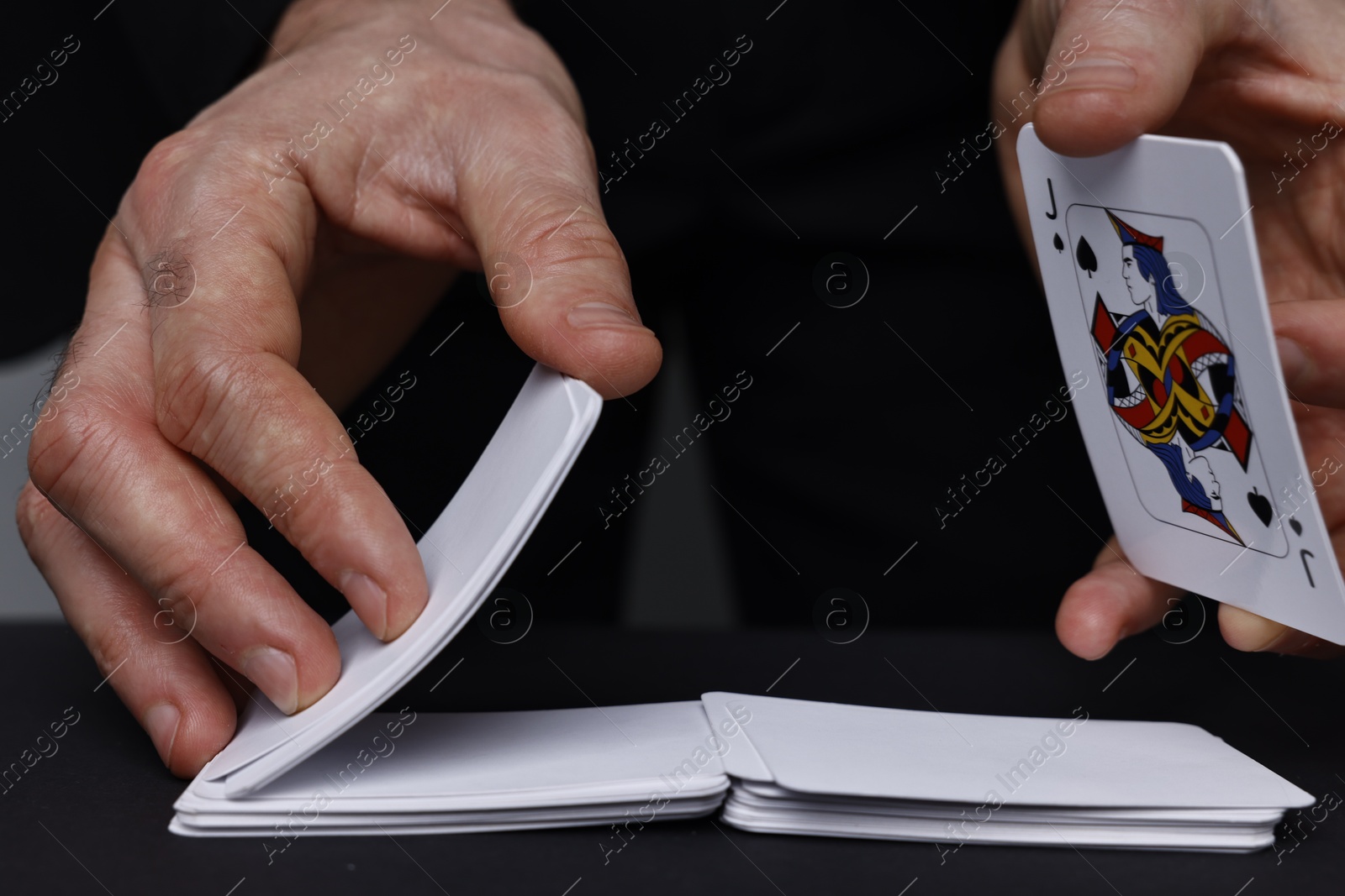 Photo of Illusionist shuffling playing cards at black table, closeup