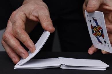 Photo of Illusionist shuffling playing cards at black table, closeup