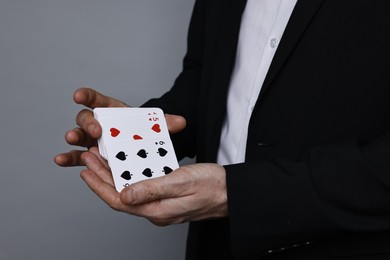 Photo of Illusionist shuffling playing cards on grey background, closeup