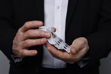 Illusionist shuffling playing cards on grey background, closeup