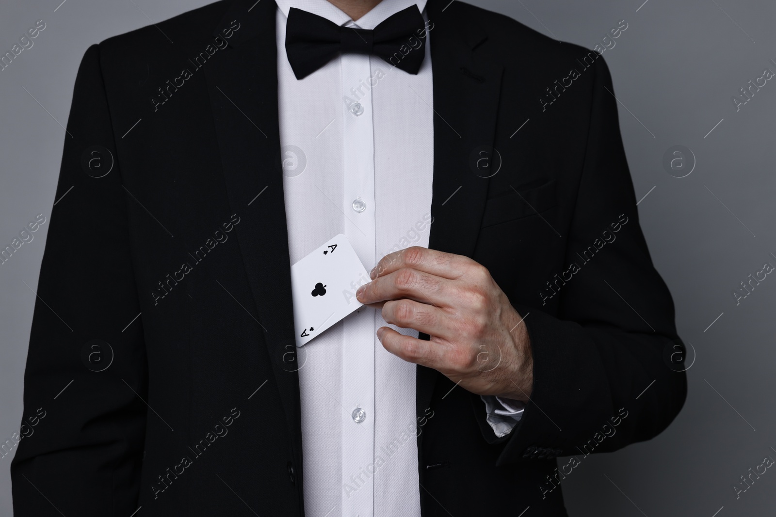 Photo of Illusionist hiding playing card behind jacket lapel on grey background, closeup