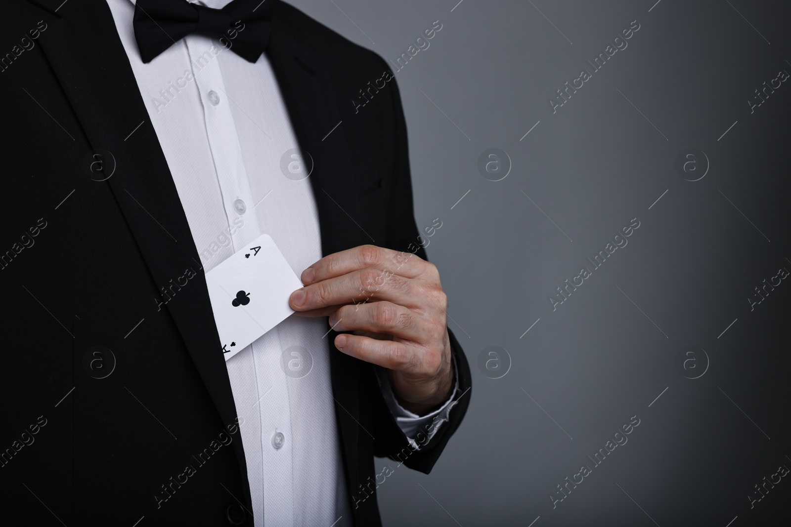 Photo of Illusionist hiding playing card behind jacket lapel on grey background, closeup. Space for text