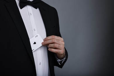 Photo of Illusionist hiding playing card behind jacket lapel on grey background, closeup. Space for text