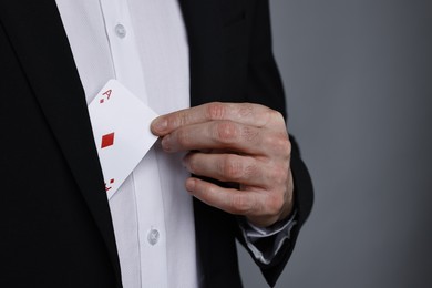 Photo of Illusionist hiding playing card behind jacket lapel on grey background, closeup