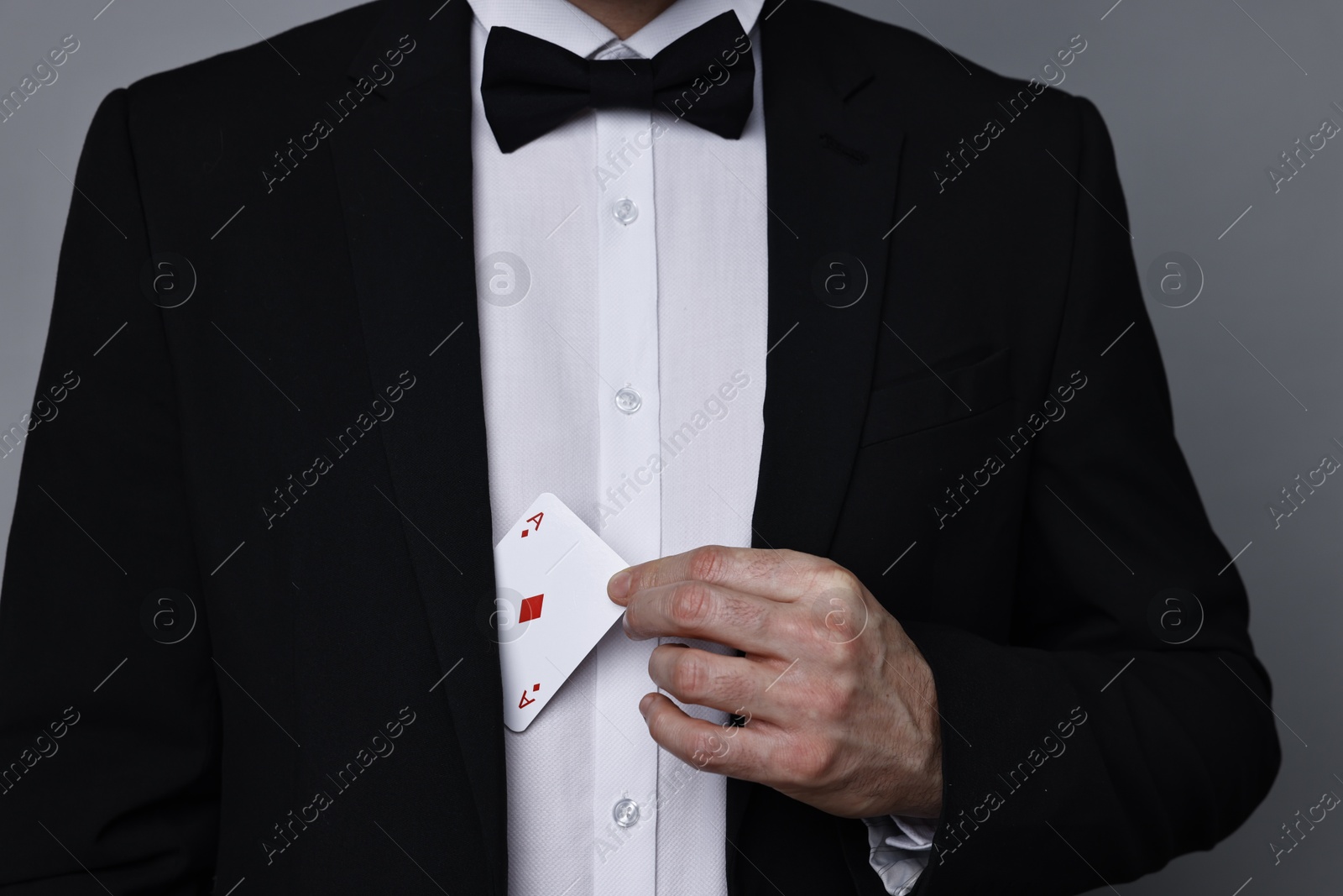 Photo of Illusionist hiding playing card behind jacket lapel on grey background, closeup