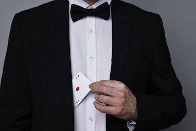 Illusionist hiding playing card behind jacket lapel on grey background, closeup