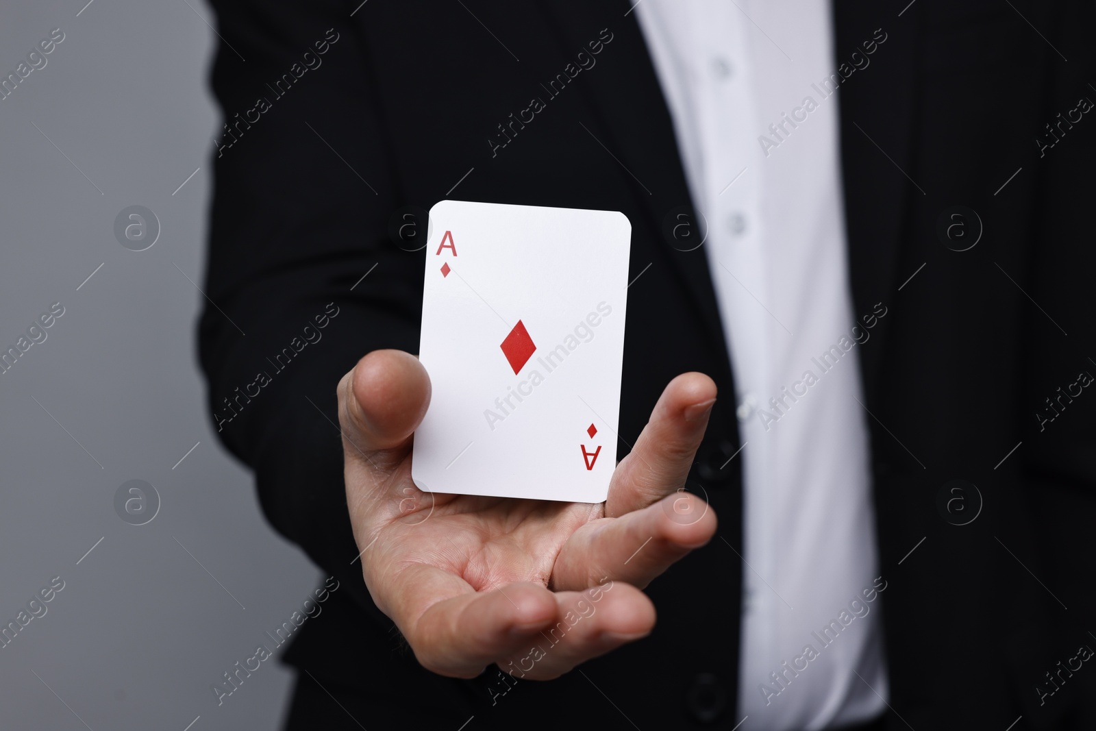 Photo of Illusionist with playing card on grey background, closeup