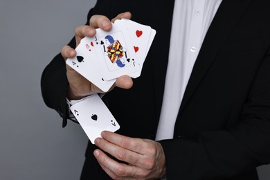 Photo of Illusionist hiding one playing card up his sleeve while showing deck on grey background, closeup