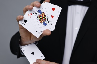 Photo of Illusionist hiding one playing card up his sleeve while showing deck on grey background, closeup