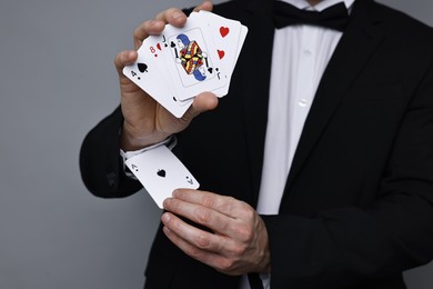 Photo of Illusionist hiding one playing card up his sleeve while showing deck on grey background, closeup