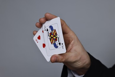 Photo of Illusionist with playing cards on grey background, closeup