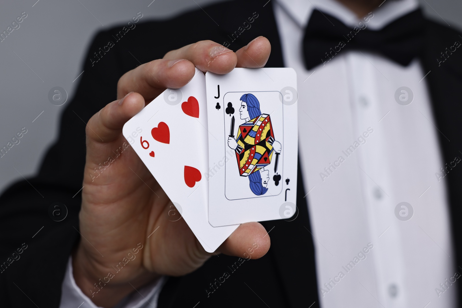 Photo of Illusionist with playing cards on grey background, closeup