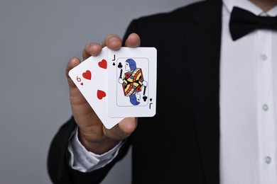 Photo of Illusionist with playing cards on grey background, closeup