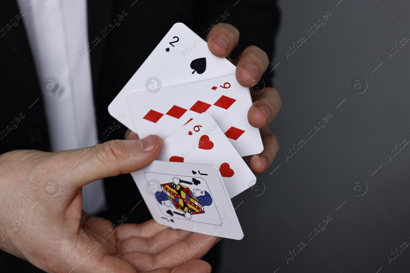 Photo of Illusionist with playing cards on grey background, closeup