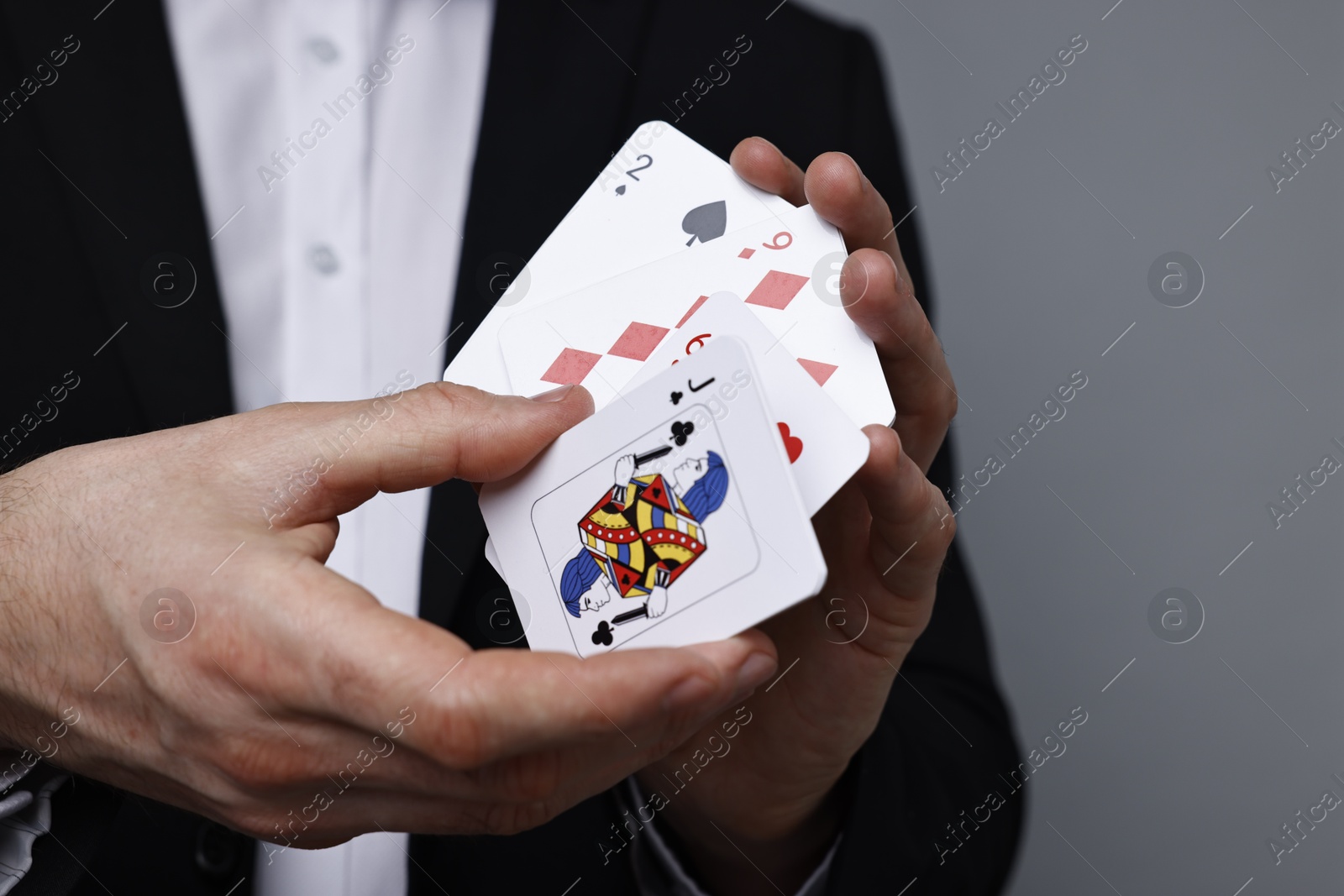 Photo of Illusionist with playing cards on grey background, closeup