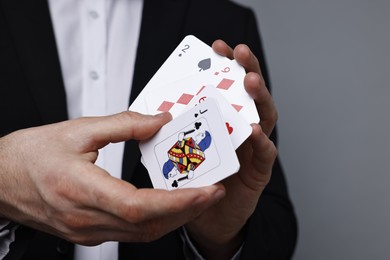 Photo of Illusionist with playing cards on grey background, closeup