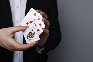 Photo of Illusionist with playing cards on grey background, closeup. Space for text